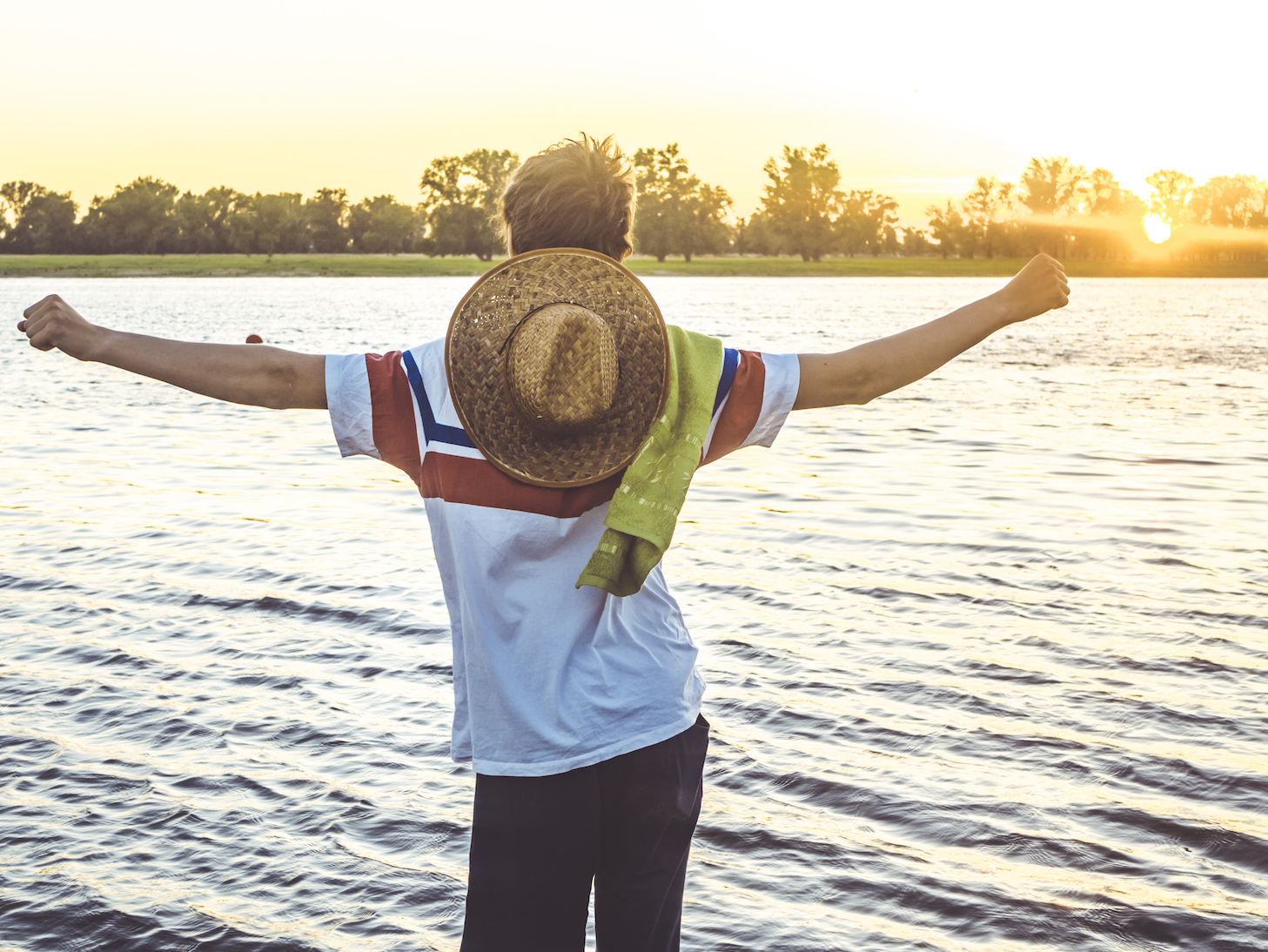 back view of young man standing in the beach water looking at the sunset